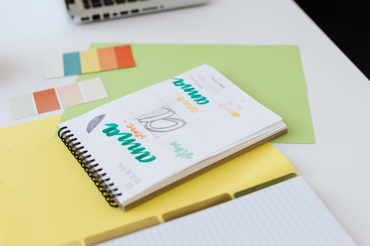 Close-up view of colorful design sketches in a spiral notebook, with color swatches laid out on a white desk.