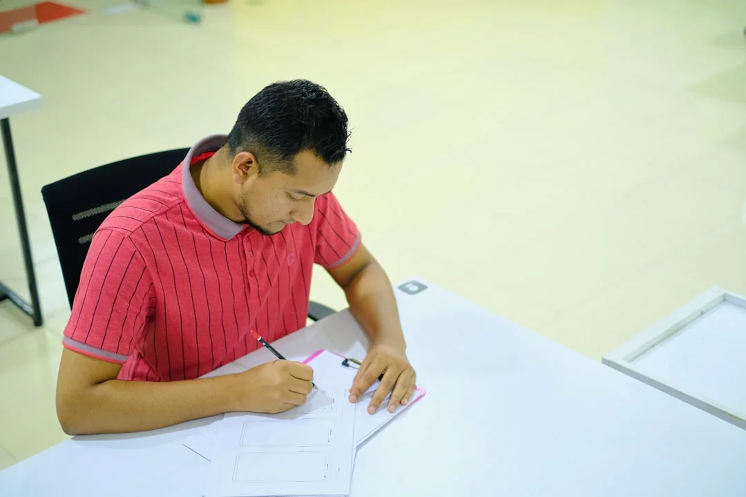 A person writing in a notebook, focusing on pencil sketching and typography design.